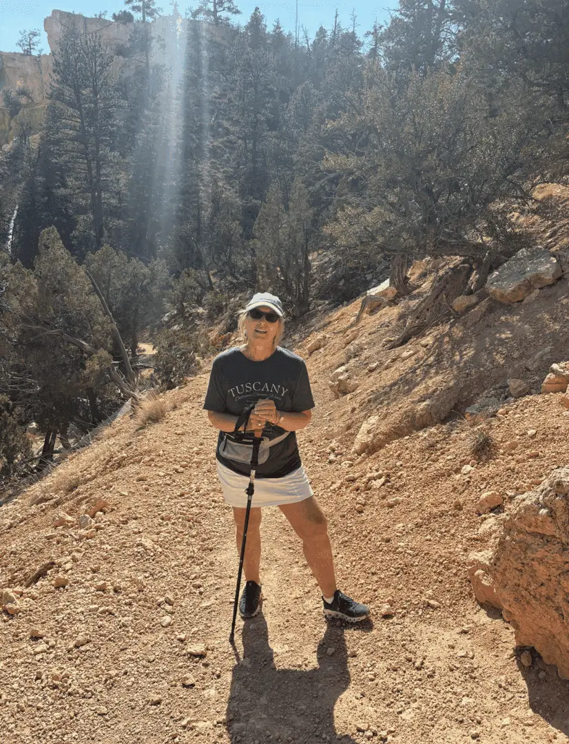 Person hiking on a sunny, rocky trail surrounded by trees.